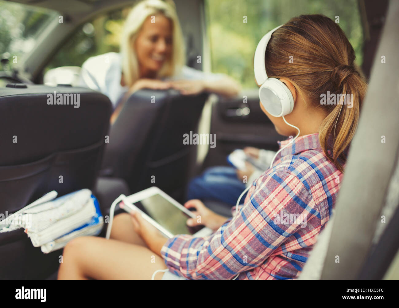 Girl with headphones using digital tablet watching video in back seat of car Stock Photo