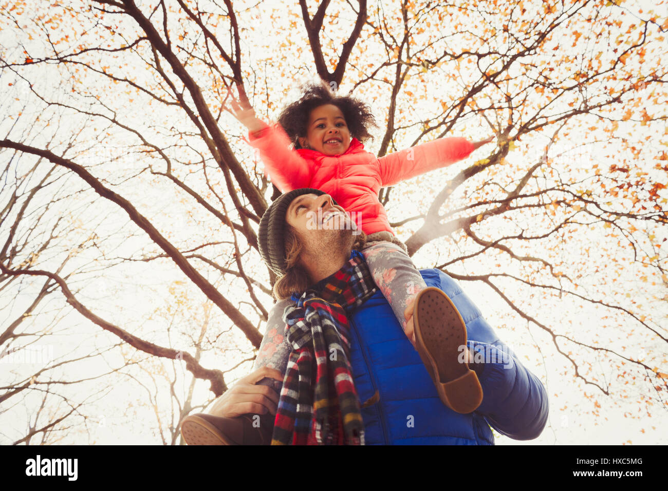 Father carrying daughter on shoulders under tree in autumn park Stock Photo