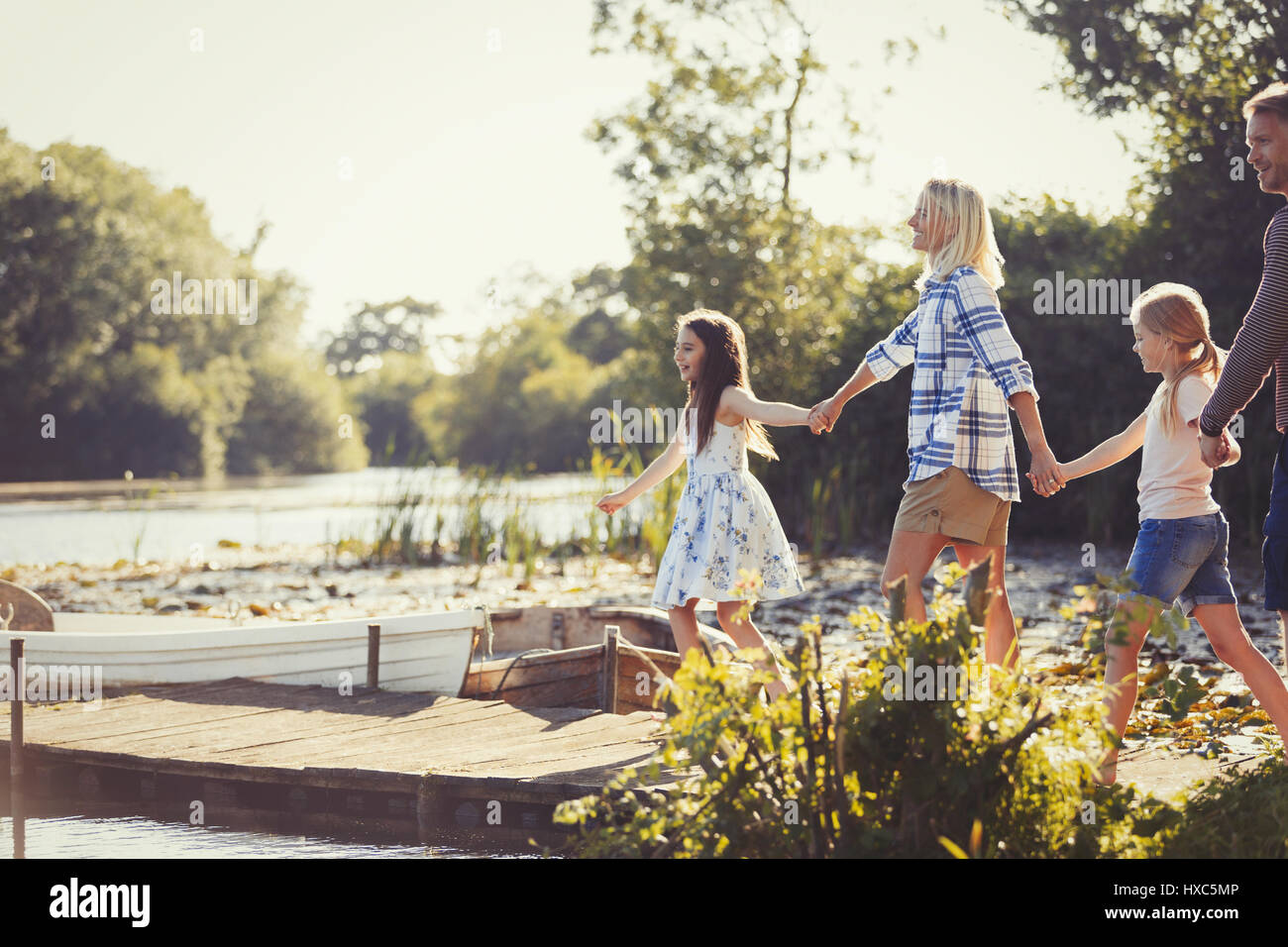 Family holding hands and walking on sunny lakeside dock Stock Photo