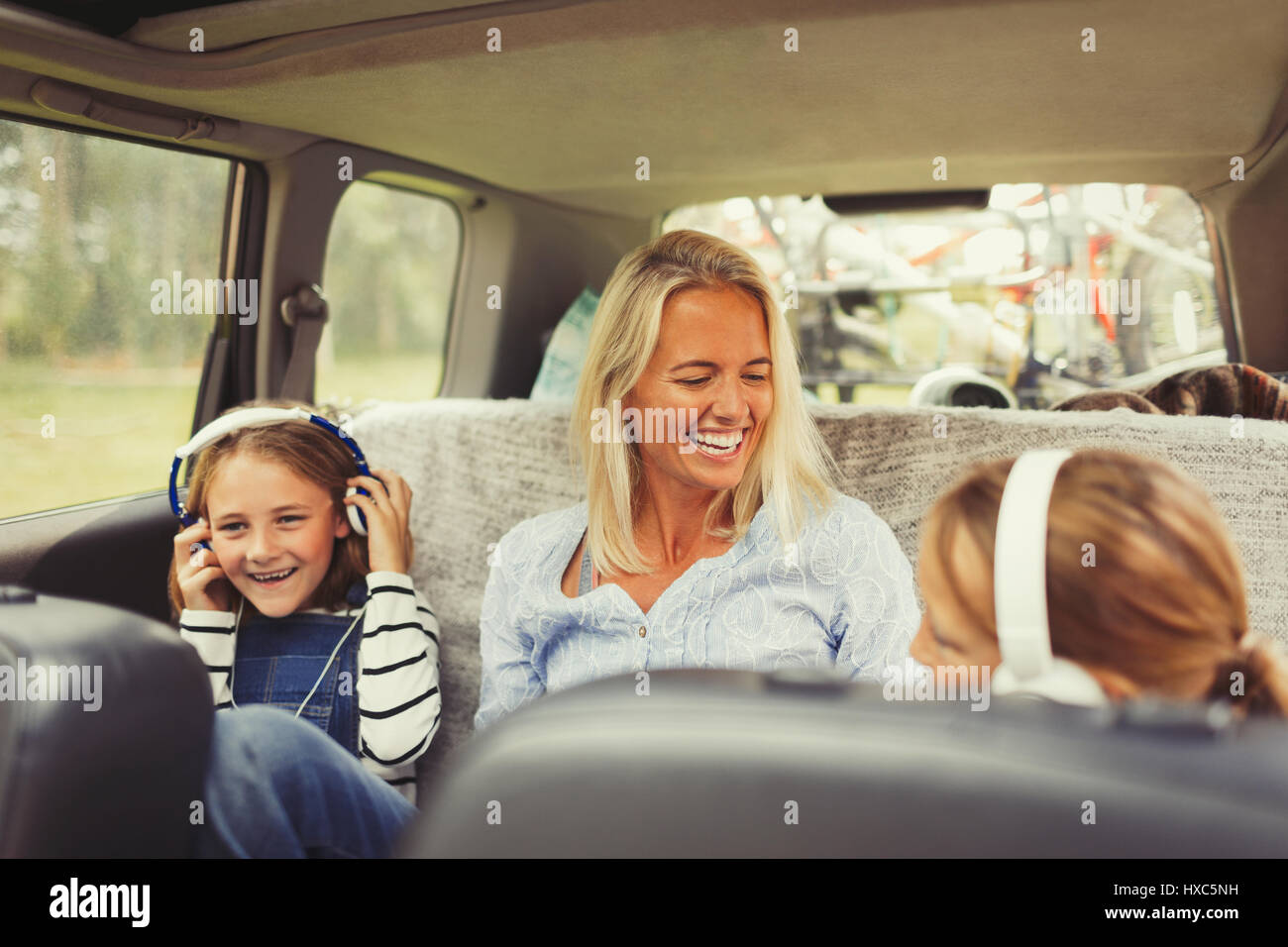 Laughing mother and daughters with headphones in back seat of car Stock Photo