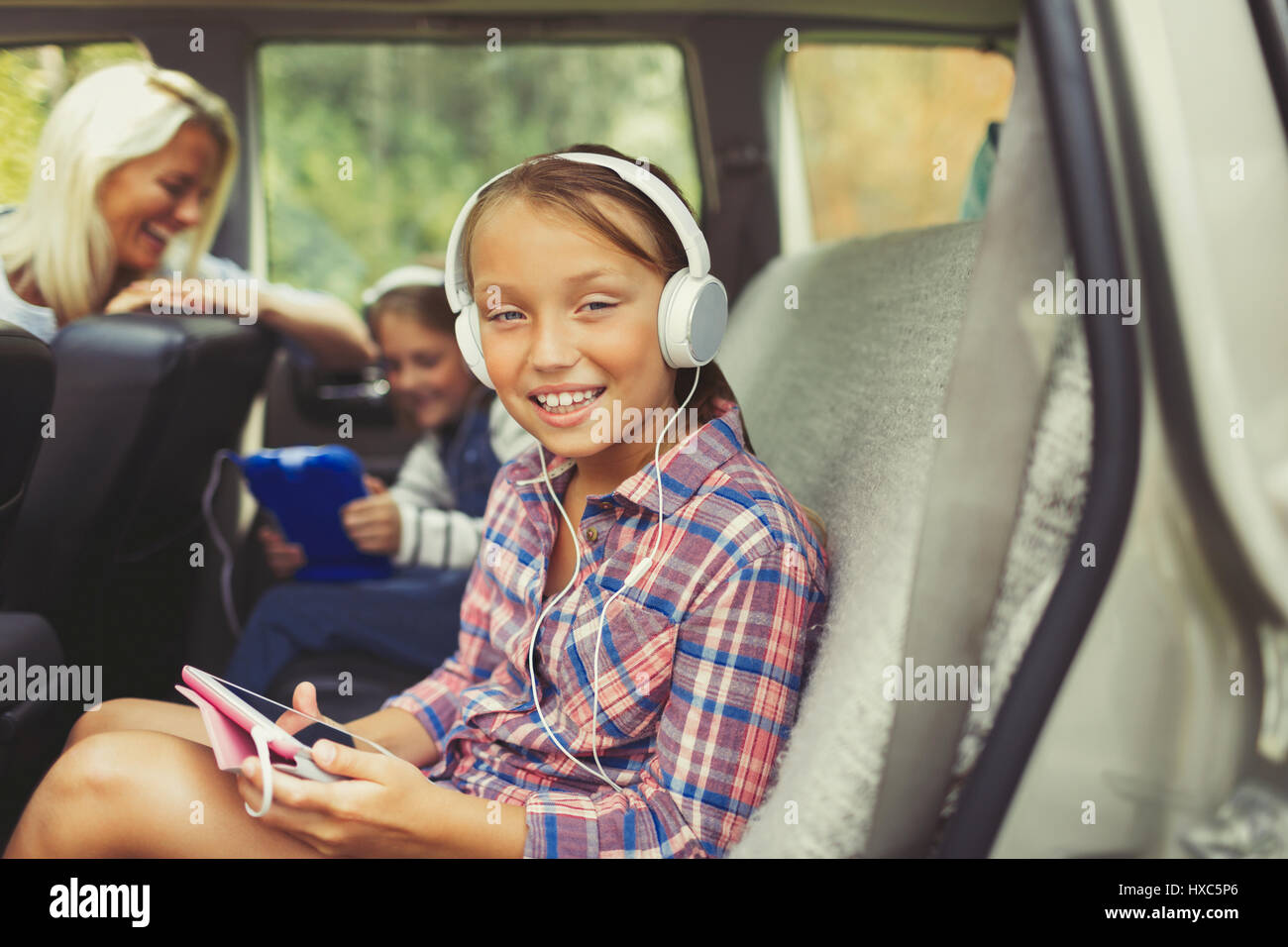 Portrait smiling girl with headphones using digital tablet in back seat of car Stock Photo