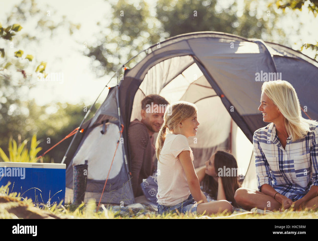 Family talking and relaxing outside tent at sunny campsite Stock Photo