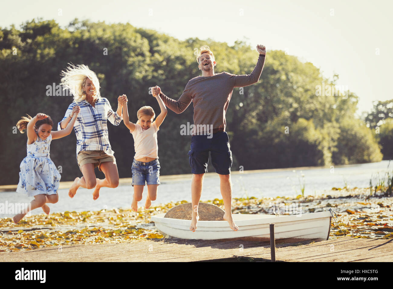 Exuberant family jumping on sunny lake dock Stock Photo