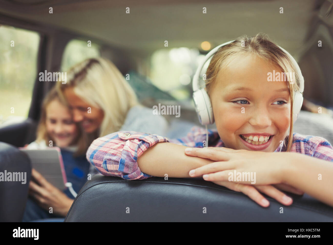 Smiling girl listening to music with headphones in back seat of car Stock Photo