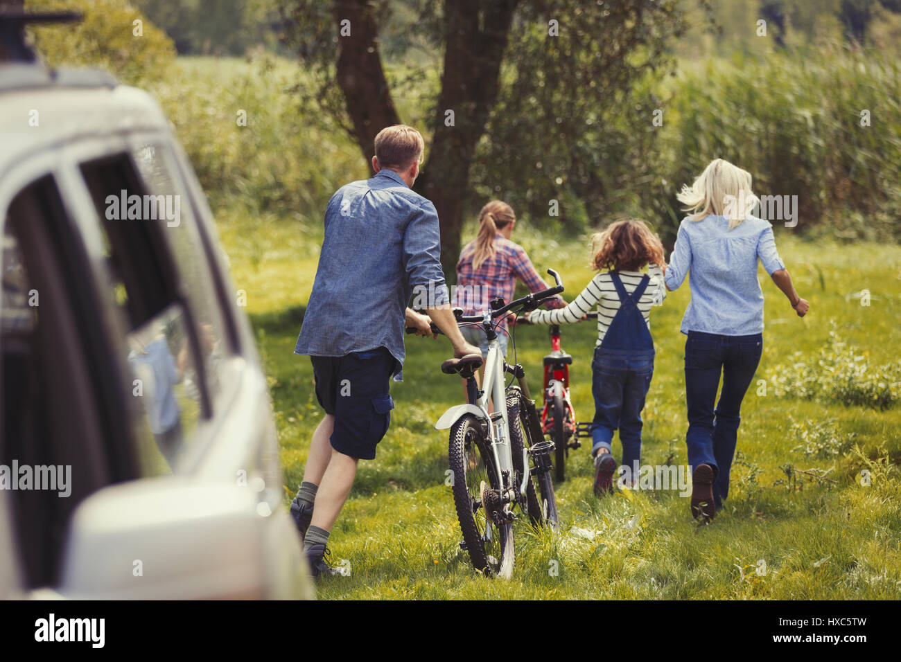 Family walking mountain bikes away from car Stock Photo
