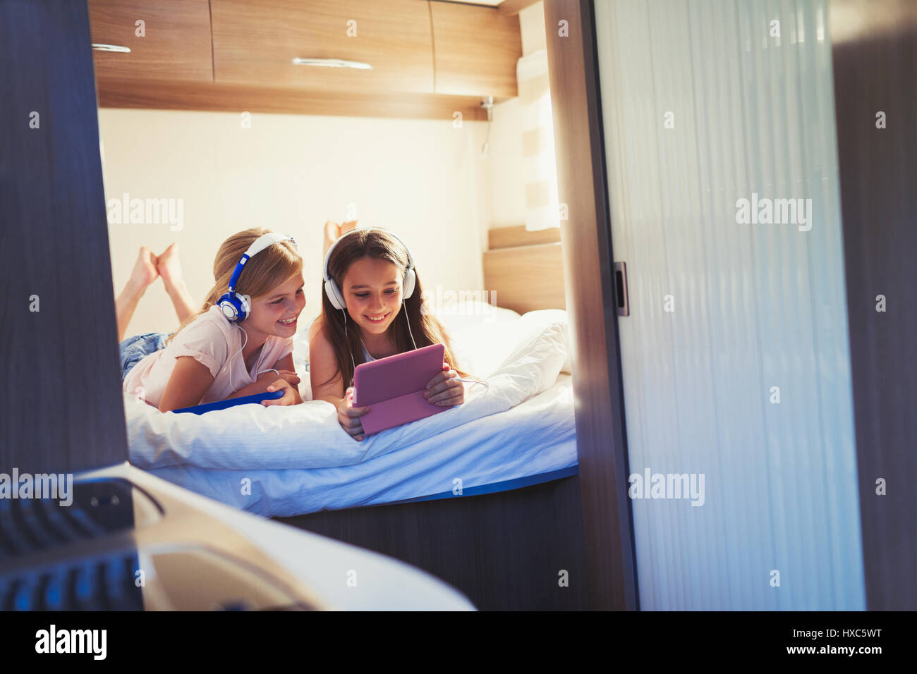 Sisters with headphones sharing digital tablet, watching video inside motor home Stock Photo