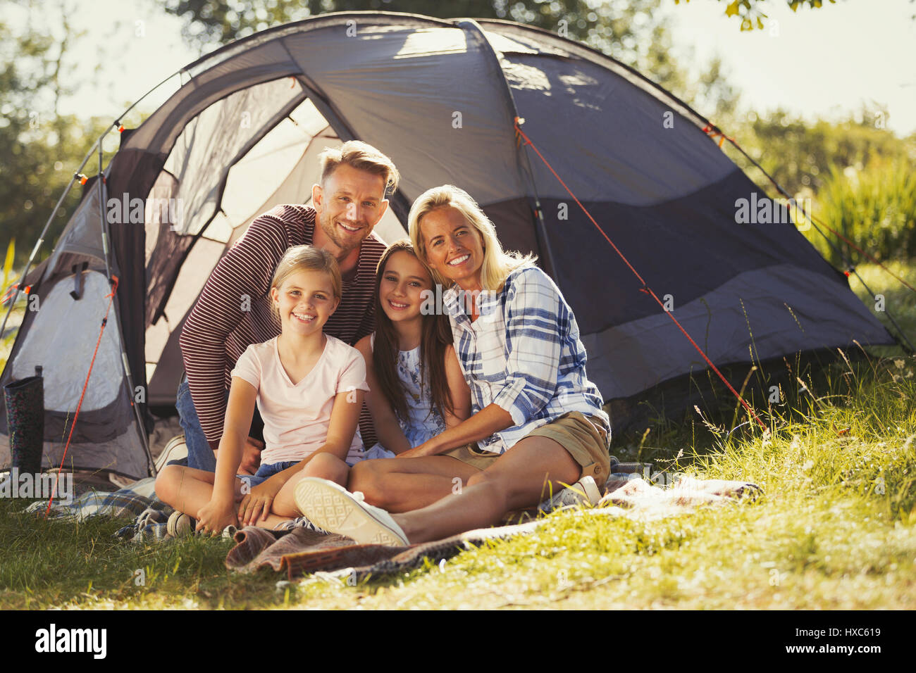 Portrait smiling family relaxing outside sunny campsite tent Stock Photo