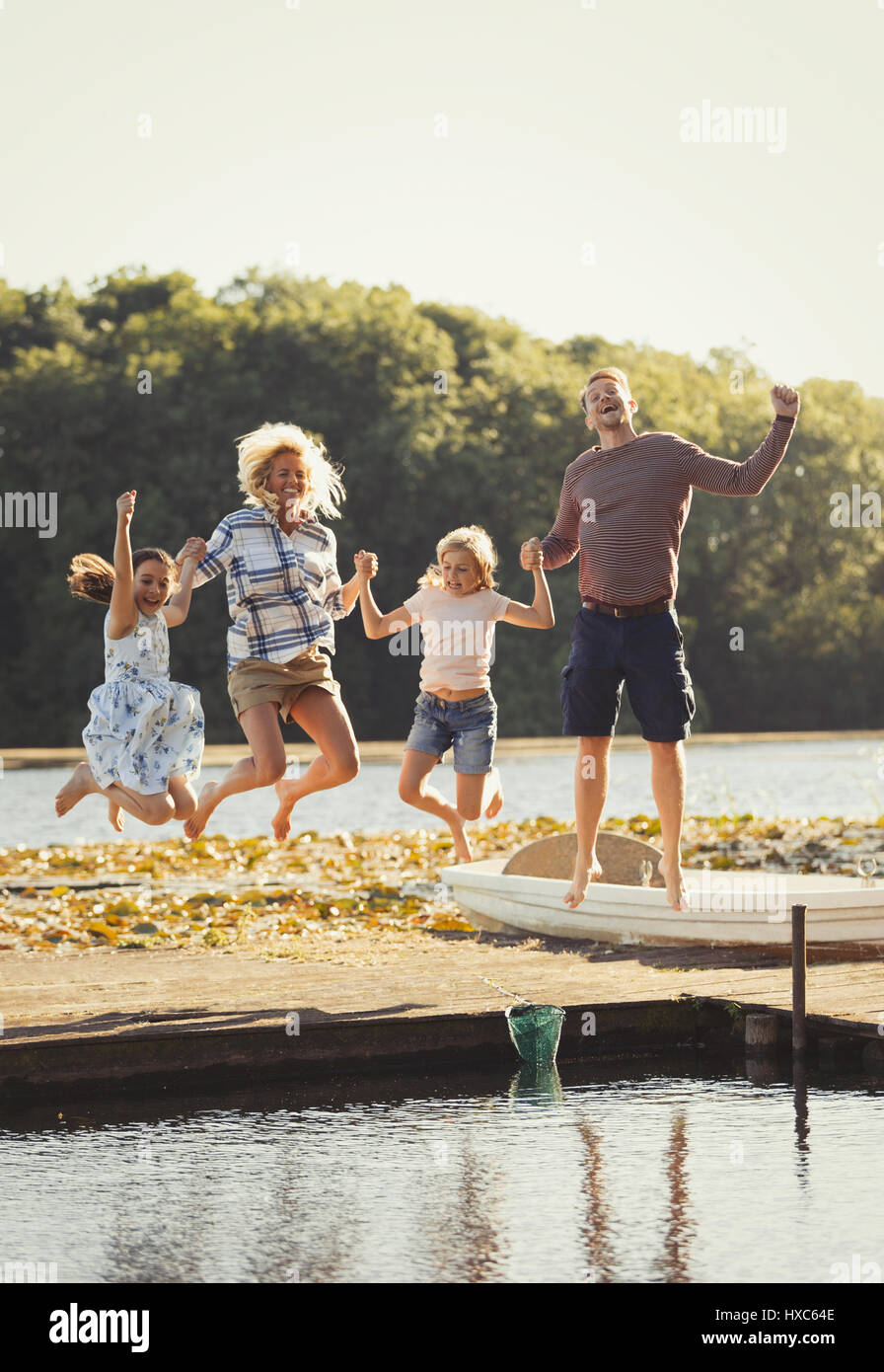 Portrait playful family jumping on sunny lake dock Stock Photo