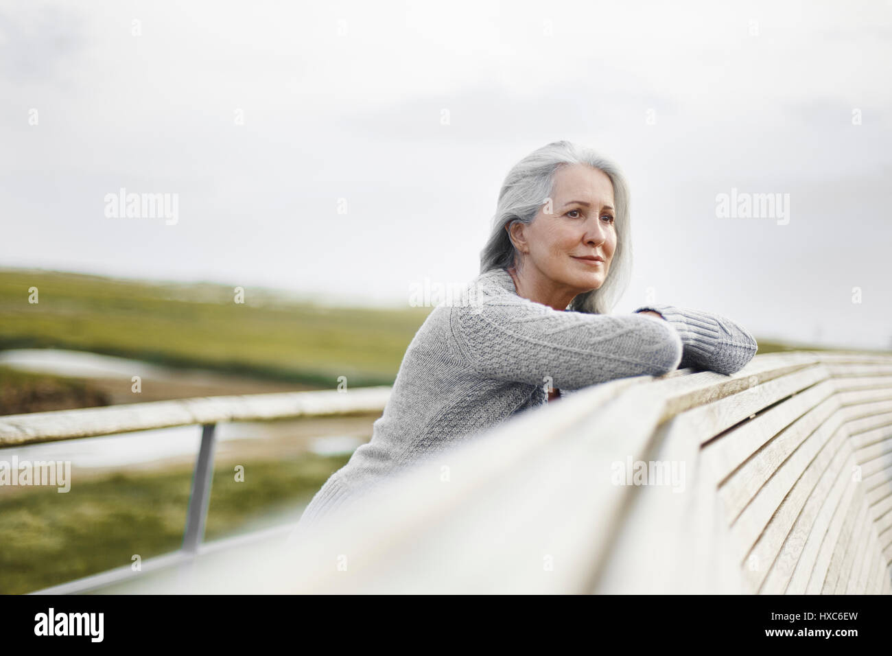 Serene senior woman leaning on boardwalk ledge Stock Photo