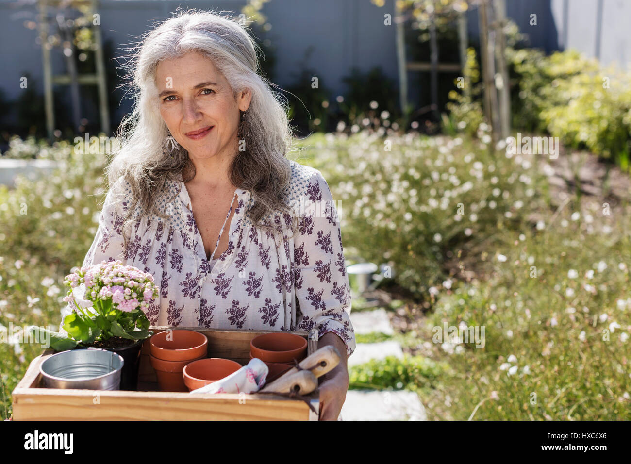 Portrait mature woman carrying gardening tray in sunny garden Stock Photo