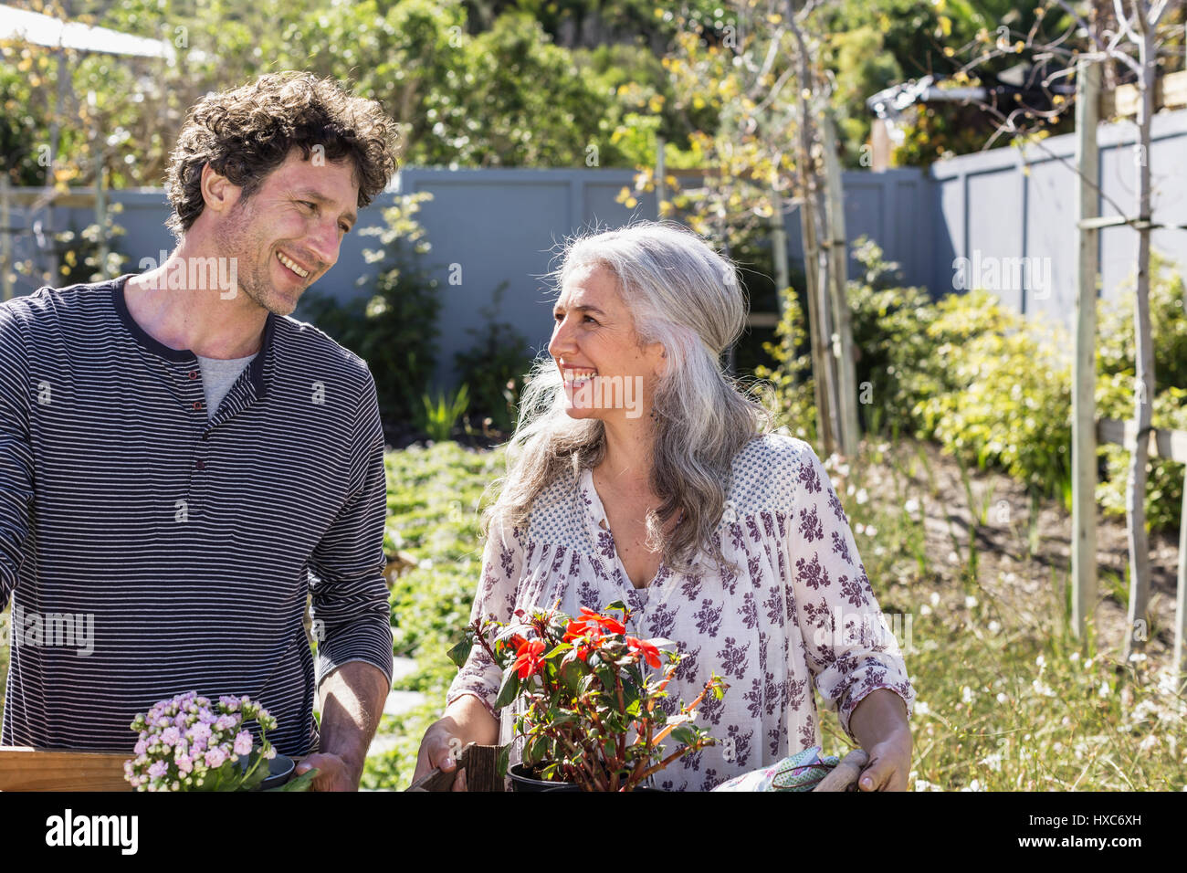 Happy couple carrying potted flowers, gardening in sunny garden Stock Photo