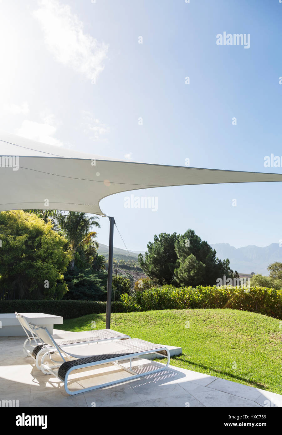 Sunny modern luxury patio with lounge chairs under awning Stock Photo