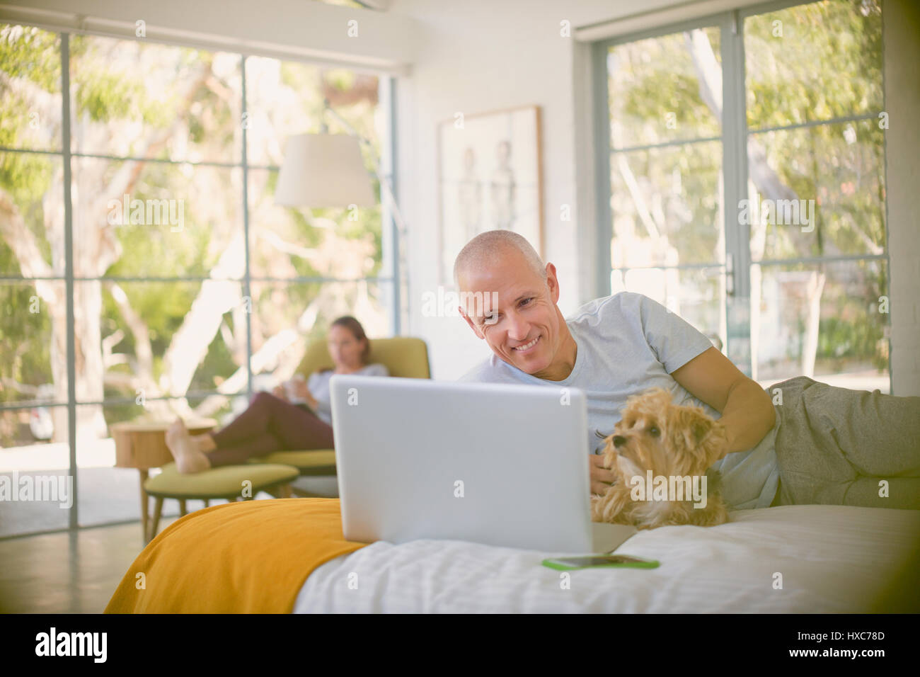 Smiling man with dog using laptop on bed Stock Photo