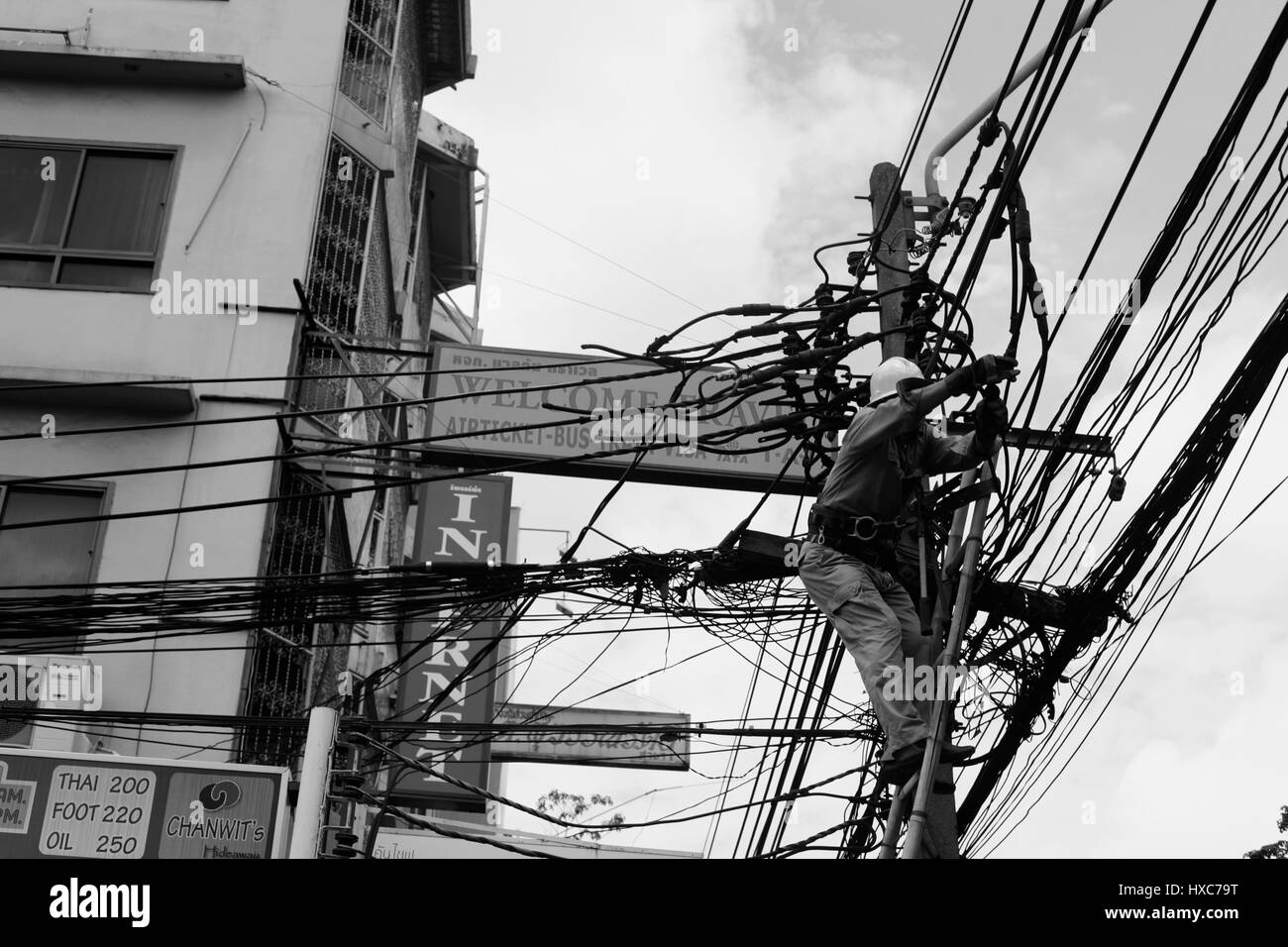 An electrician is maintaining the twisted lines of electricity wires on the street somewhere in Thailand. Stock Photo