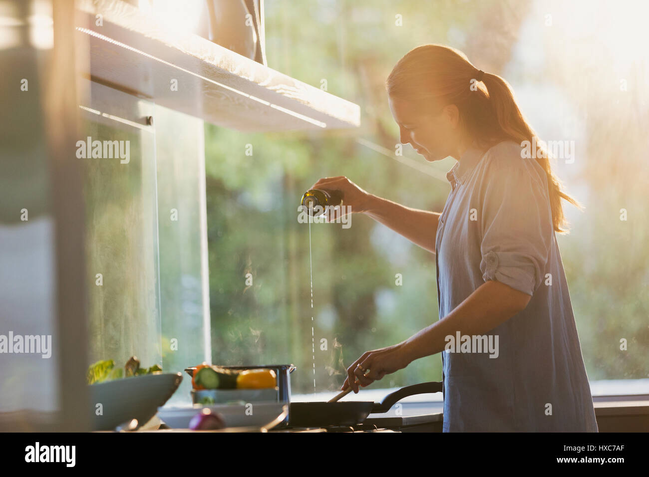 Woman pouring oil into pan on stove in kitchen Stock Photo