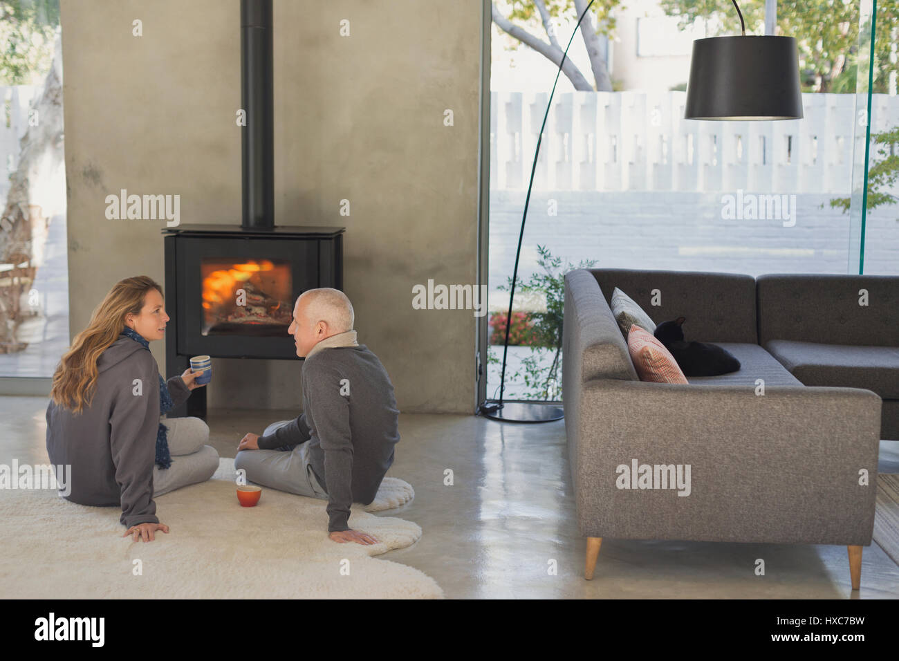 Couple Drinking Tea And Talking In Front Of Wood Stove Fireplace