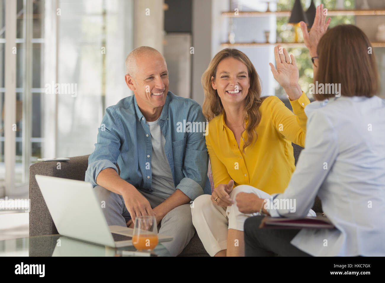 Happy couple high fiving financial advisor in living room Stock Photo