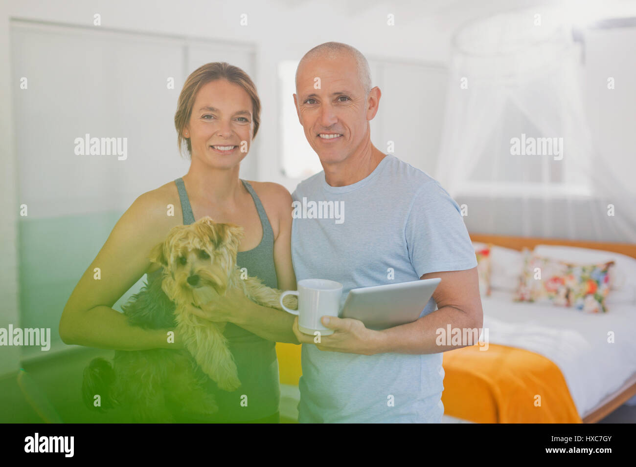 Portrait smiling mature couple with dog and digital tablet in bedroom Stock Photo