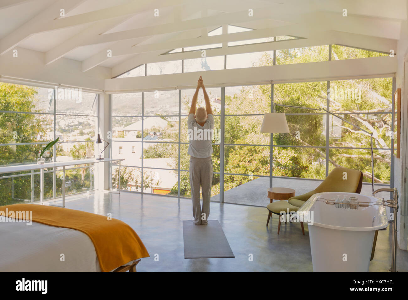 Mature man practicing yoga with hands clasped overhead in luxury bedroom Stock Photo