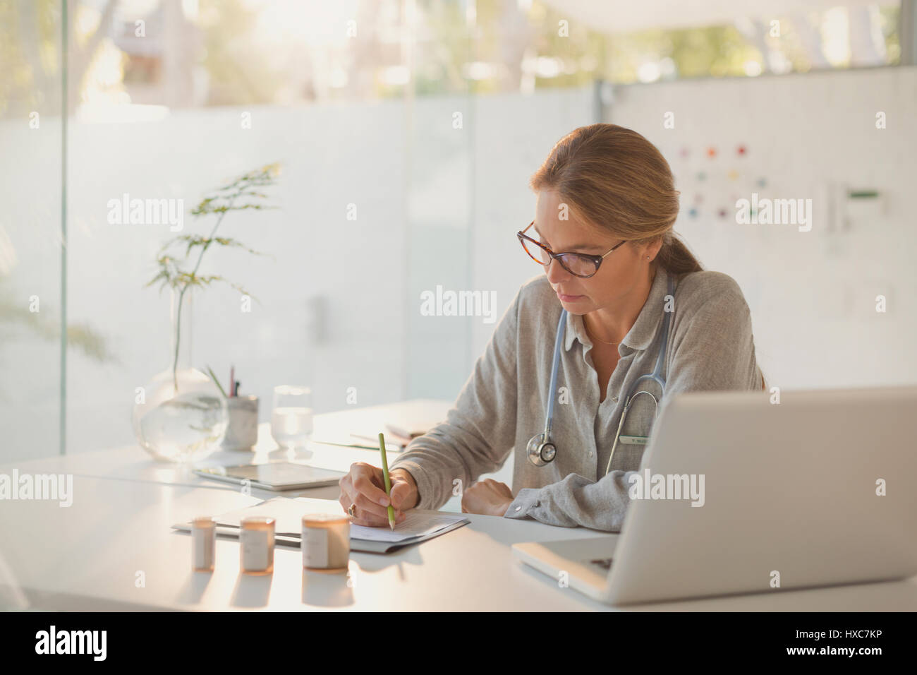 Female doctor writing prescriptions at desk in doctor’s office Stock Photo