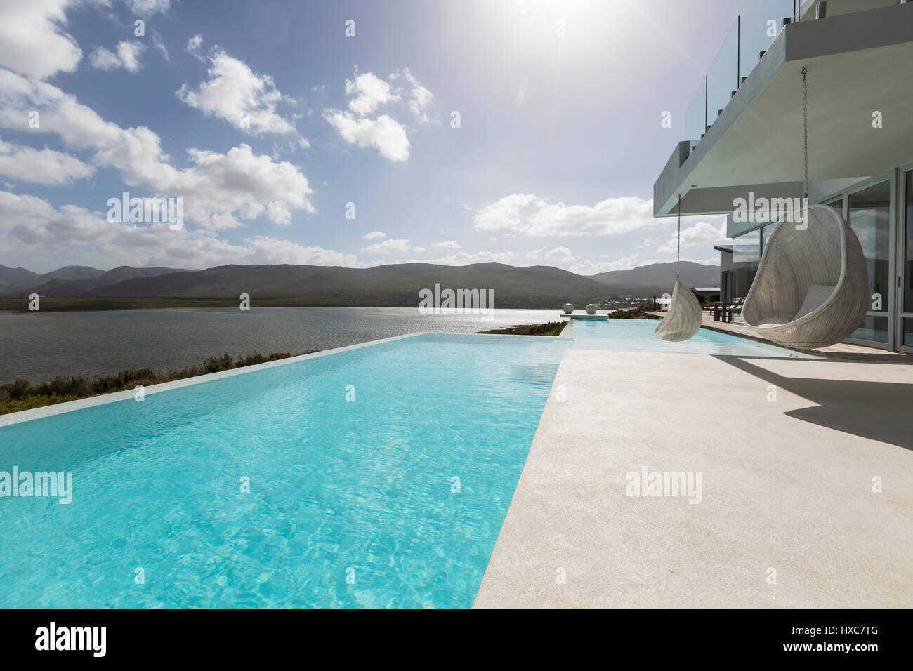 Sunny tranquil modern luxury home showcase exterior patio with infinity ...