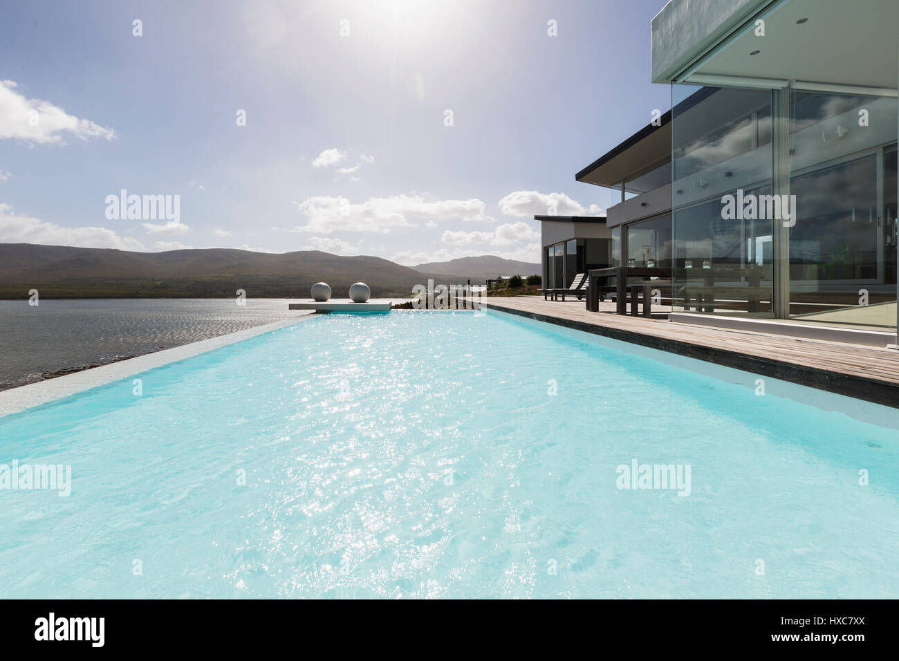 Sunny tranquil modern luxury home showcase exterior with infinity pool ...