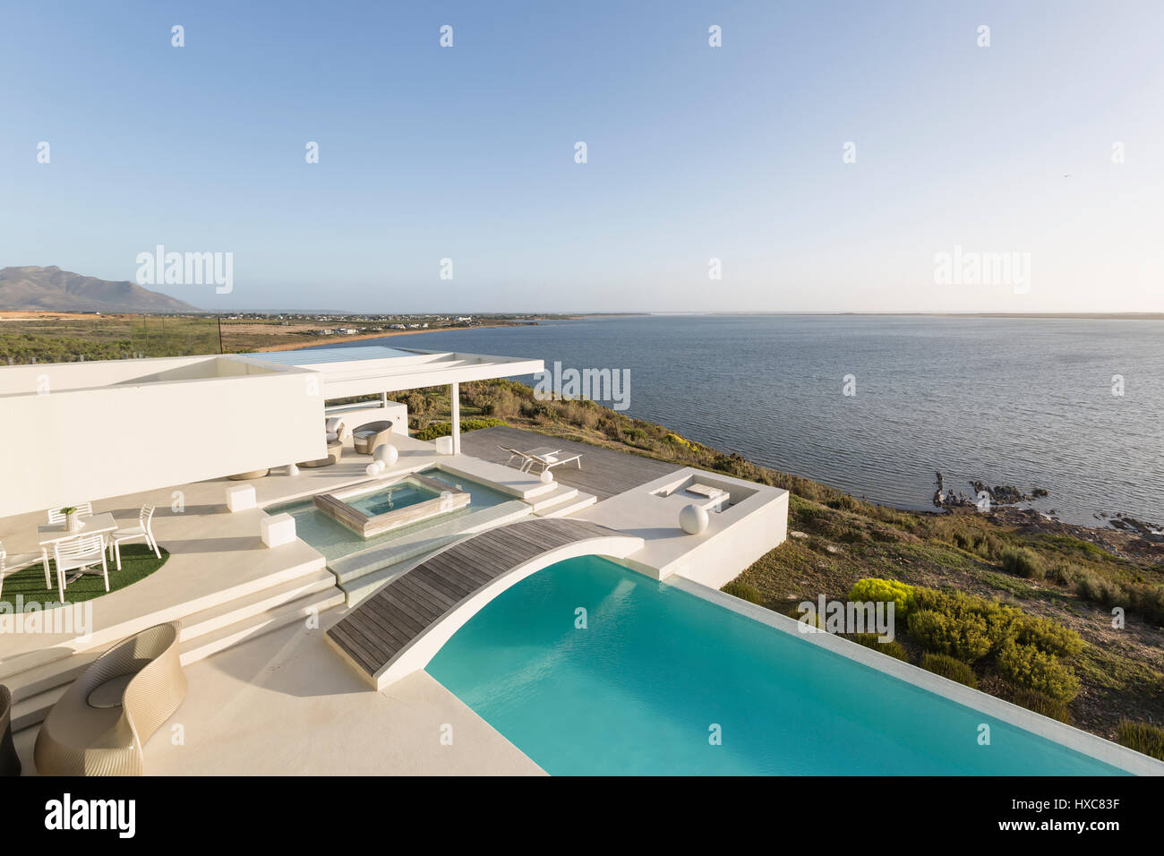 Sunny, tranquil modern luxury home showcase exterior with infinity pool ...