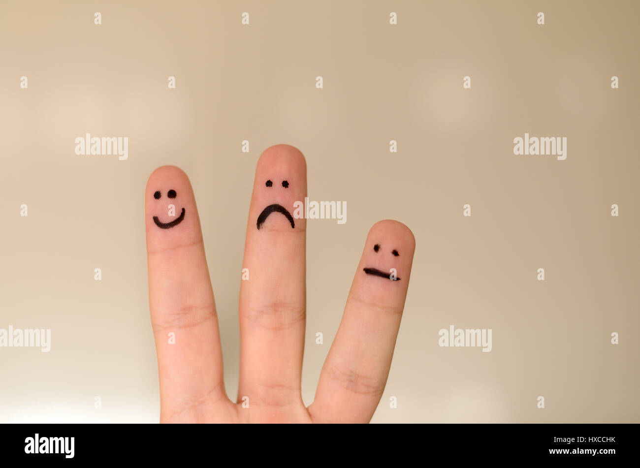 Three different emoticons hand drawn on fingers with a black marker pen with a happy smiling face, unhappy sad face and calm unemotional face isolated Stock Photo