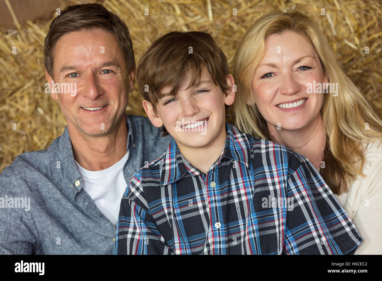 Portrait shot of an attractive, successful and happy family, middle aged man and woman couple with young boy child son sitting smiling together on hay Stock Photo