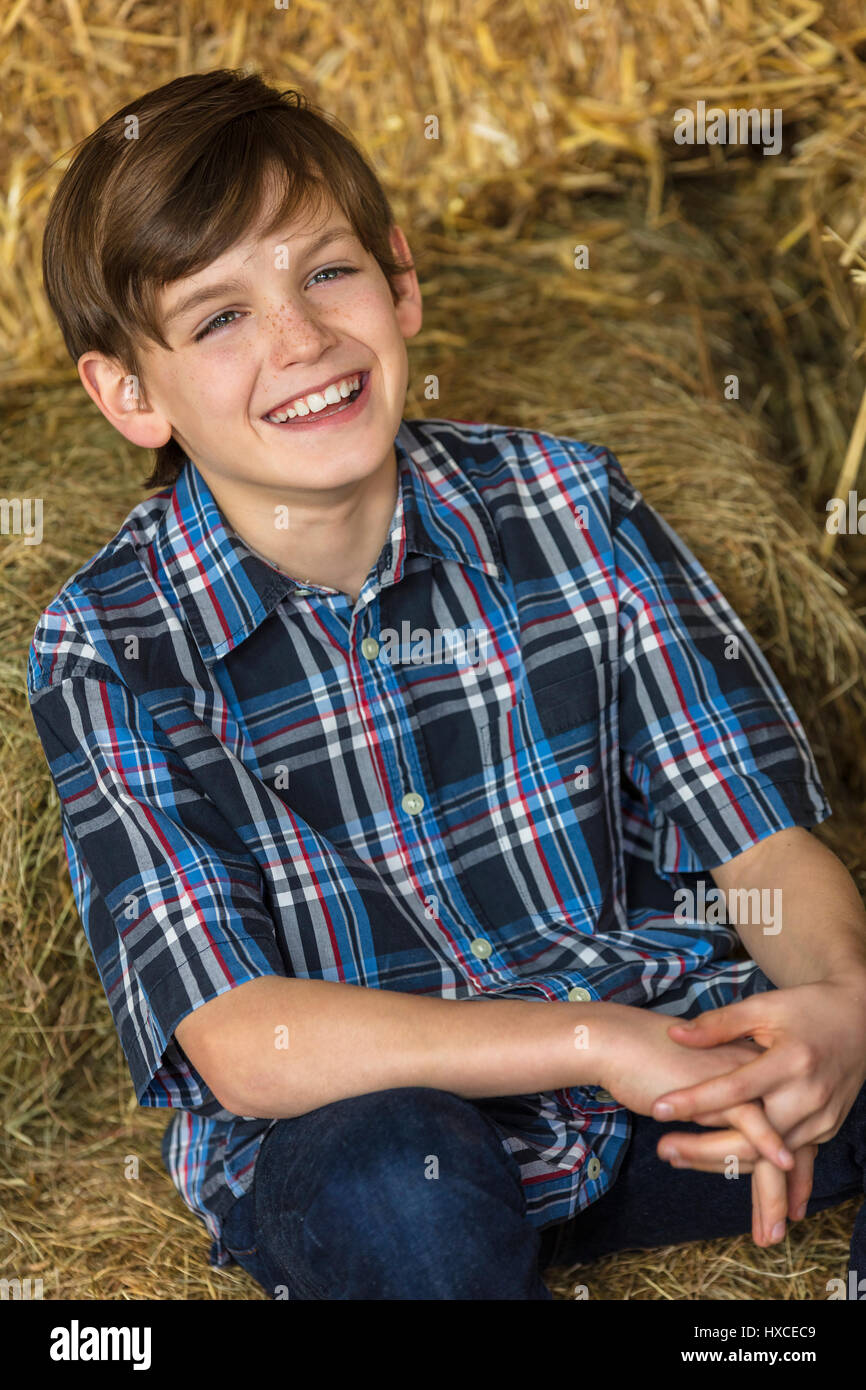 Young happy boy wearing a plaid shirt and sitting on bales of hay or straw with a toothy smile Stock Photo