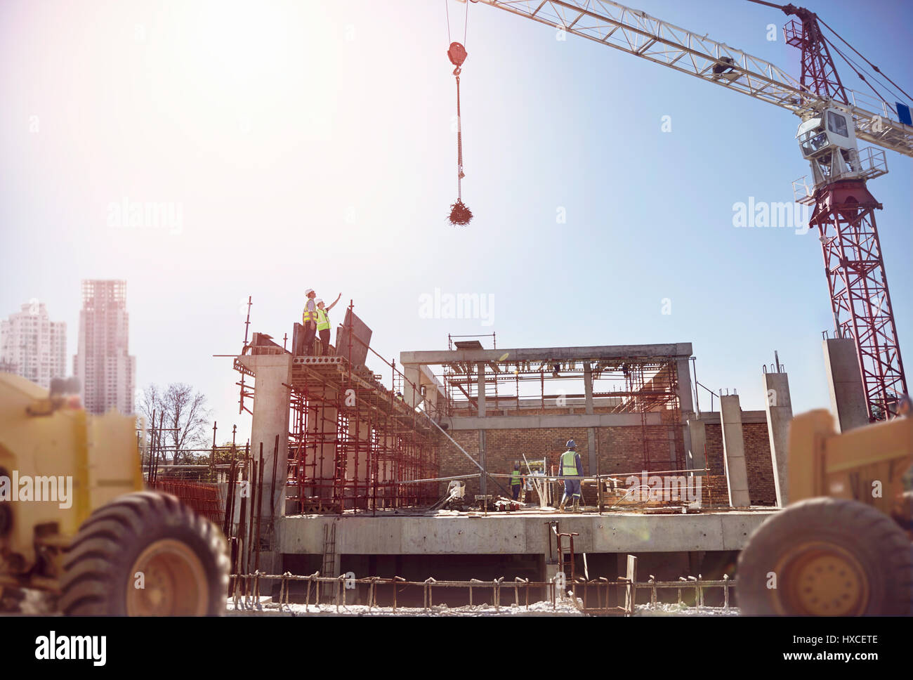 Crane over construction workers at sunny construction site Stock Photo