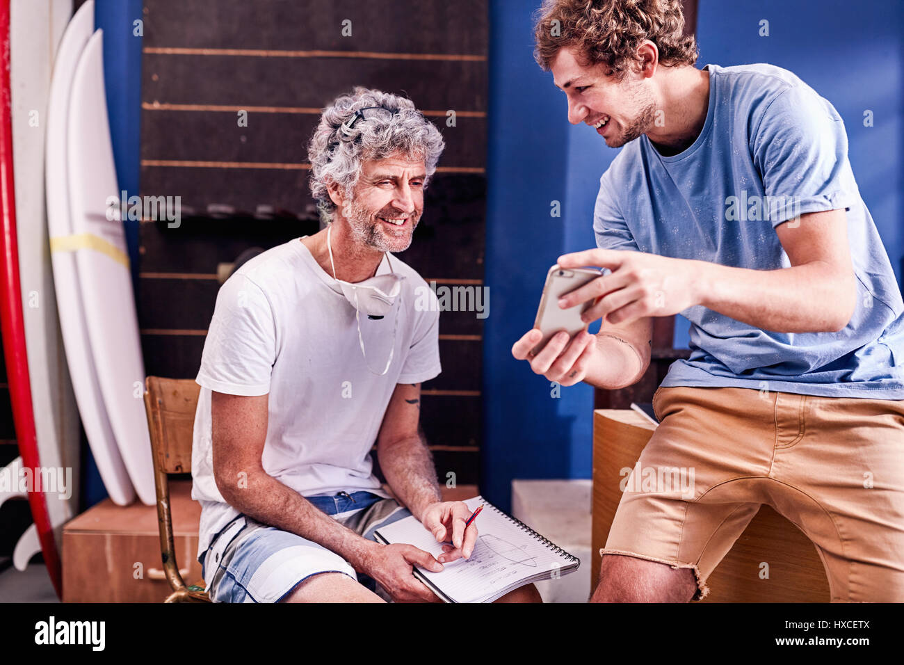 Male surfboard designers with cell phone brainstorming in workshop Stock Photo