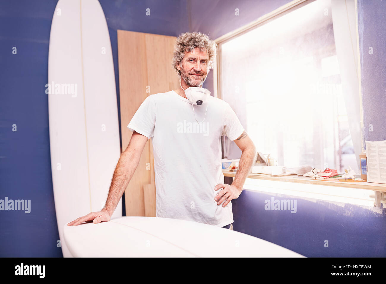 Portrait confident male surfboard designer sanding surfboard in workshop Stock Photo
