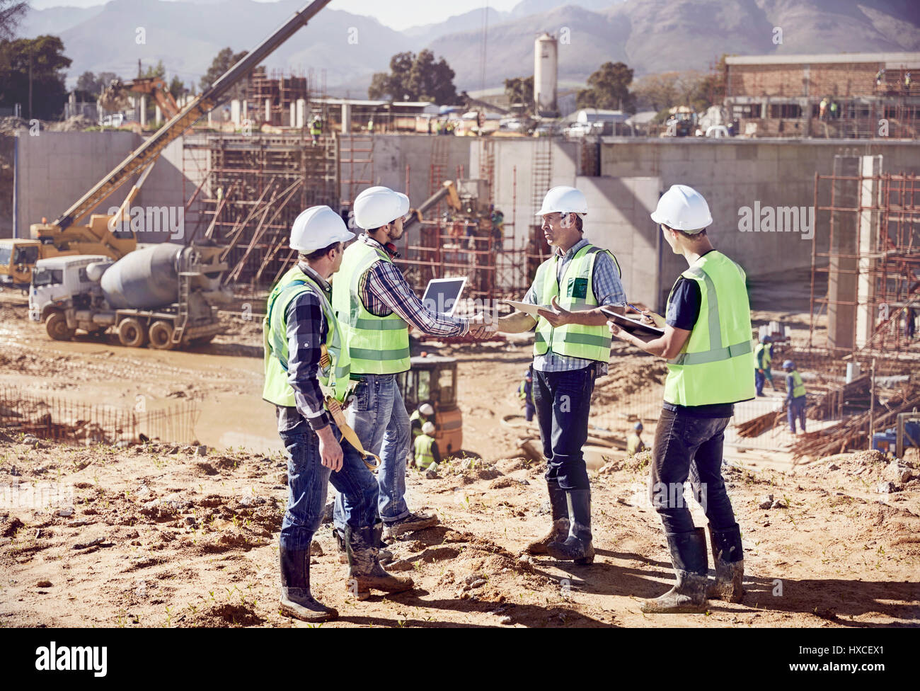 Construction workers and engineers shaking hands, meeting at sunny construction site Stock Photo