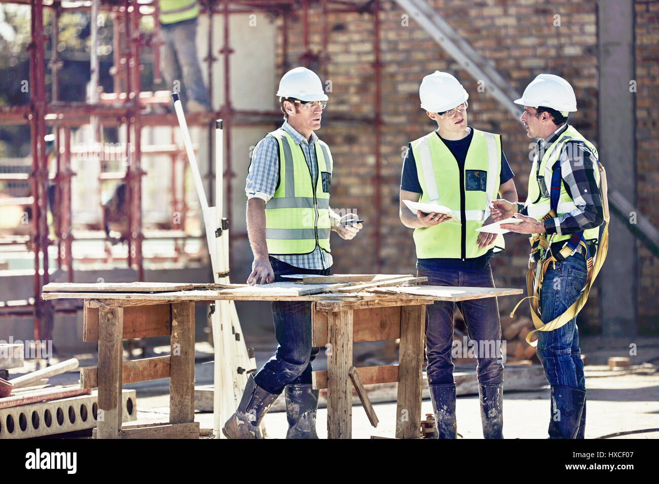 Construction workers and foreman talking at sunny construction site Stock Photo