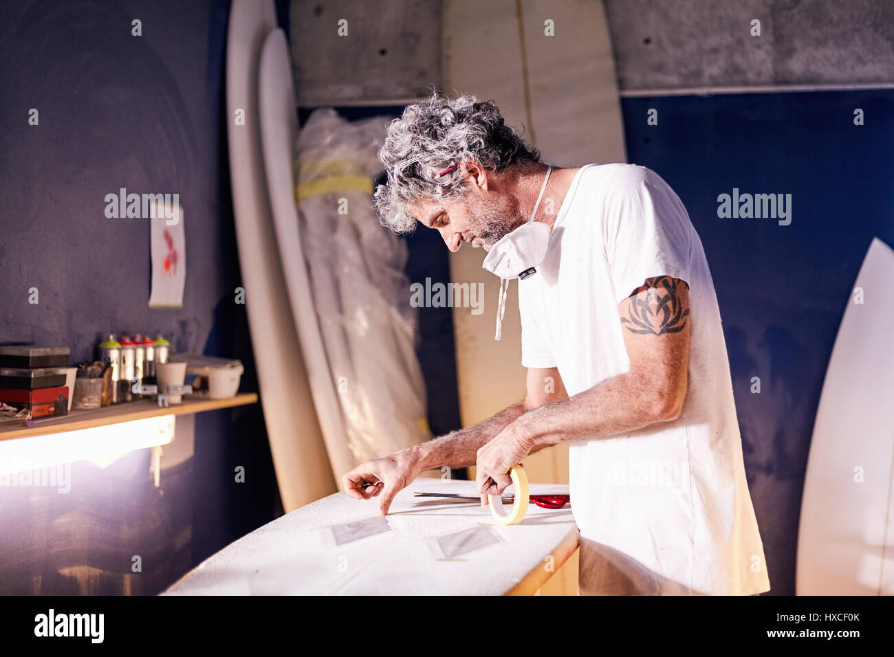 Surfboard designer taping surfboard in workshop Stock Photo