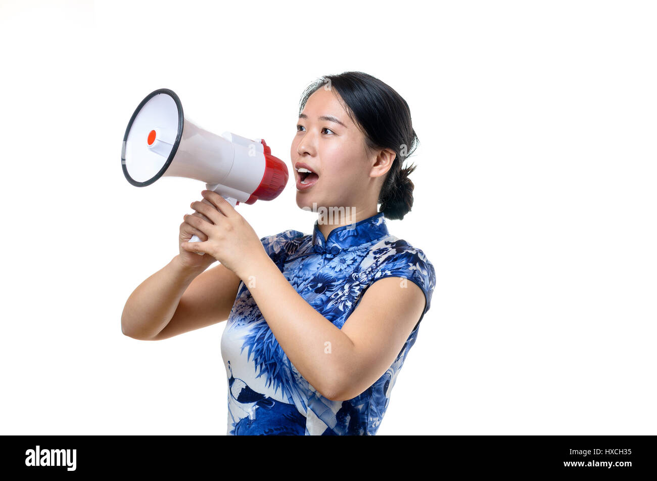 Attractive Chinese woman in traditional dress shouting into a loud hailer or megaphone at a rally or demonstration or when addressing a crowd public s Stock Photo