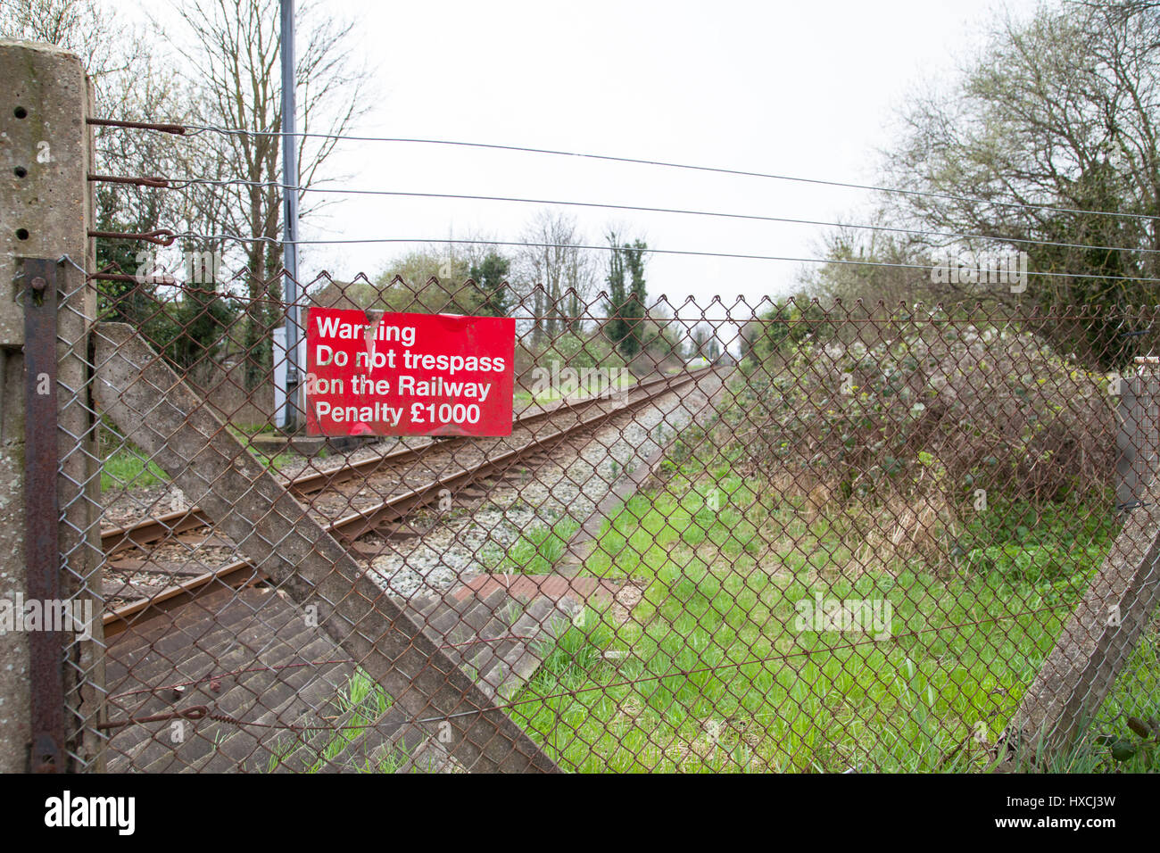 warning do not trespass on the railway penalty £1000 sign hanging on steel wire fencing with railway tracks in the background, uk Stock Photo