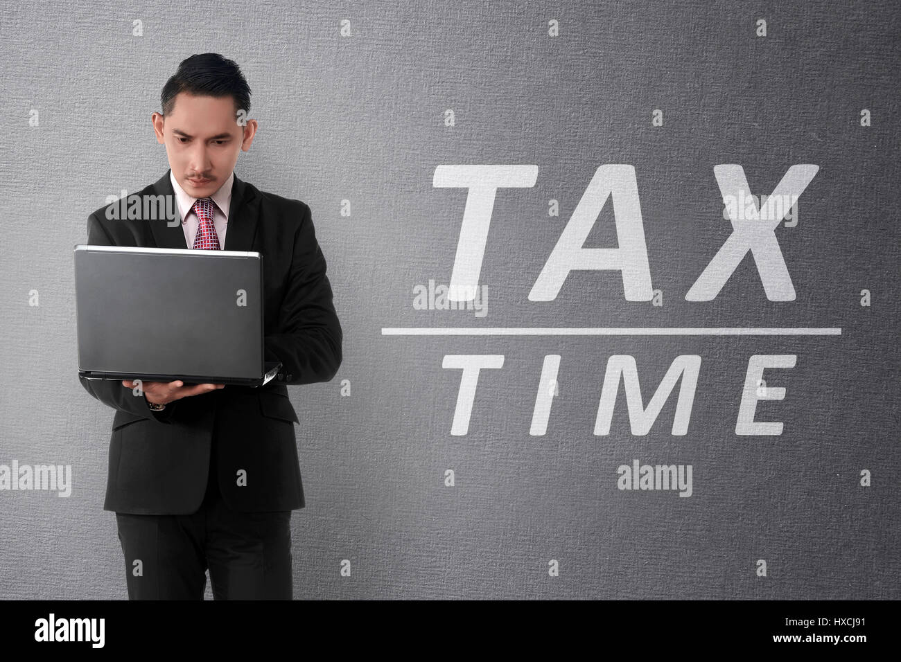 Young asian businessman working on laptop with TAX TIME text on the wall Stock Photo