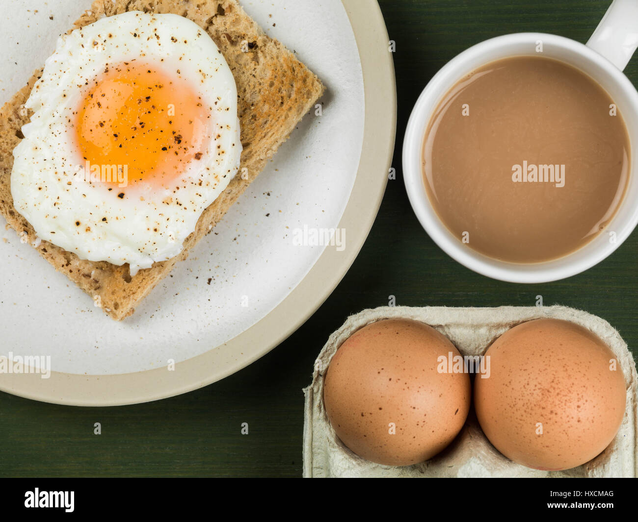 Flat Lay Composition And Tight Crop Of A Poached Egg On Toast, Sunny Side Up, Breakfast With a Mug of Tea or Coffee and Two Raw Eggs In Their Shells Stock Photo