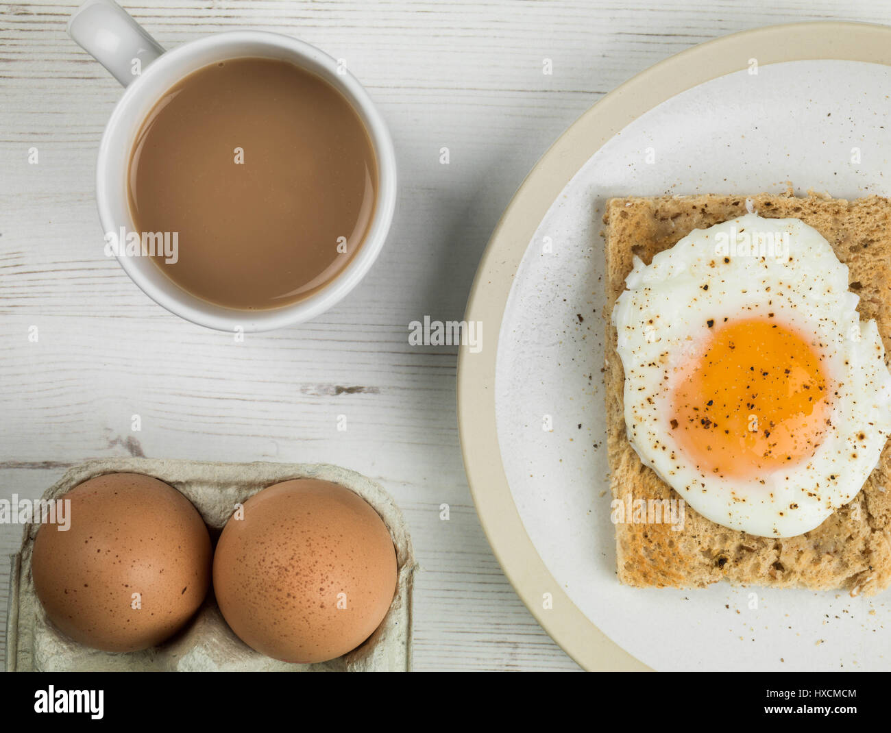 Flat Lay Composition And Tight Crop Of A Poached Egg On Toast, Sunny Side Up, Breakfast With a Mug of Tea or Coffee and Two Raw Eggs In Their Shells Stock Photo