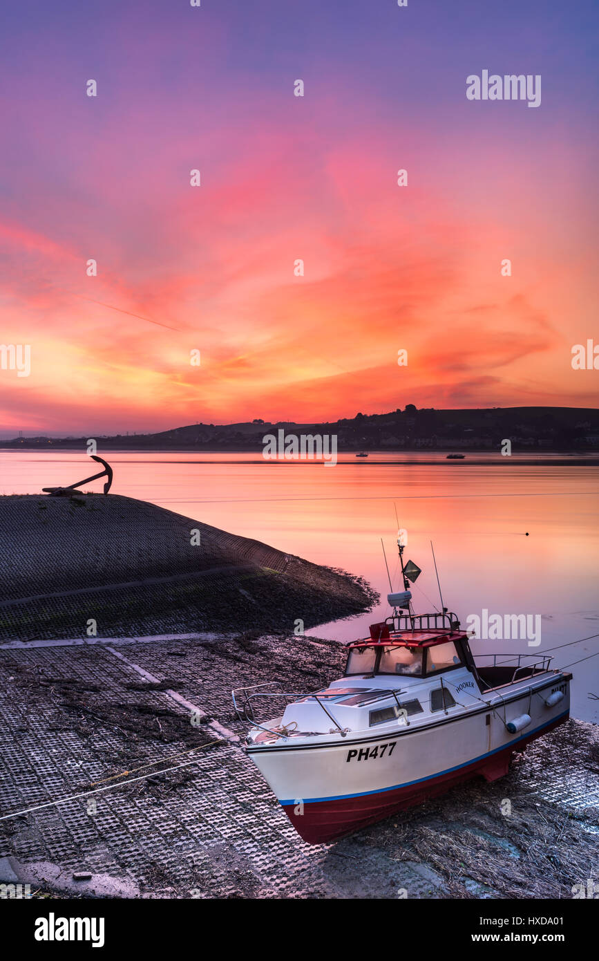 The sky turns pink over the River Torridge, as the sun rises at dawn behind Instow, lighting up a boat moored on the quay at Appledore in North Devon. Stock Photo