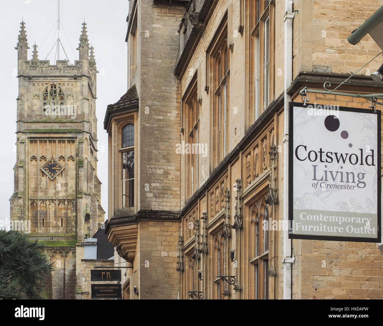 a tight shot of architecture in Cirencester with St John the Baptist and Cotswold Living hanging shop sign in the foreground, UK Stock Photo