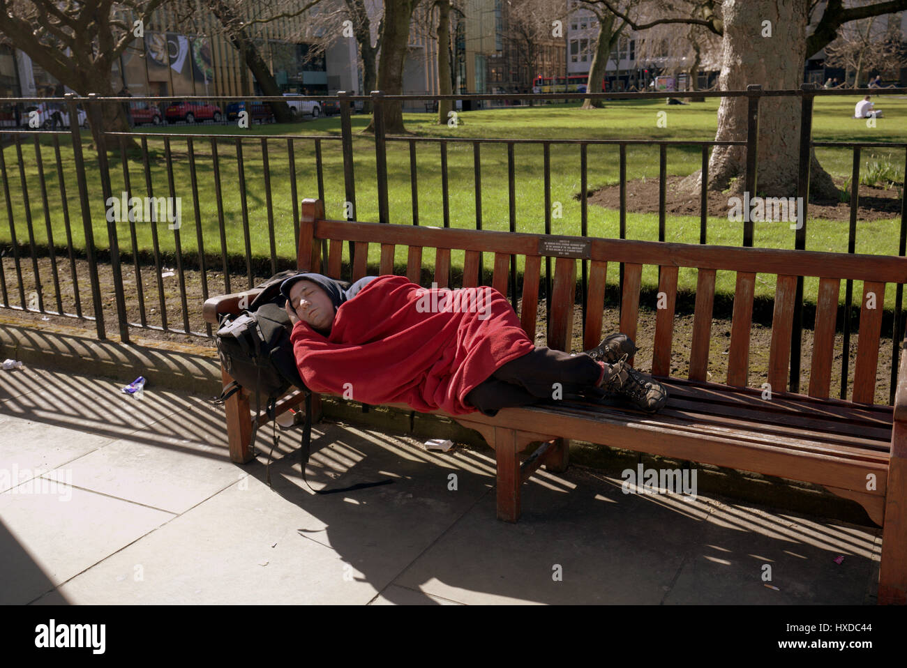man sleeping om Edinburgh park bench om the street during the day Stock Photo