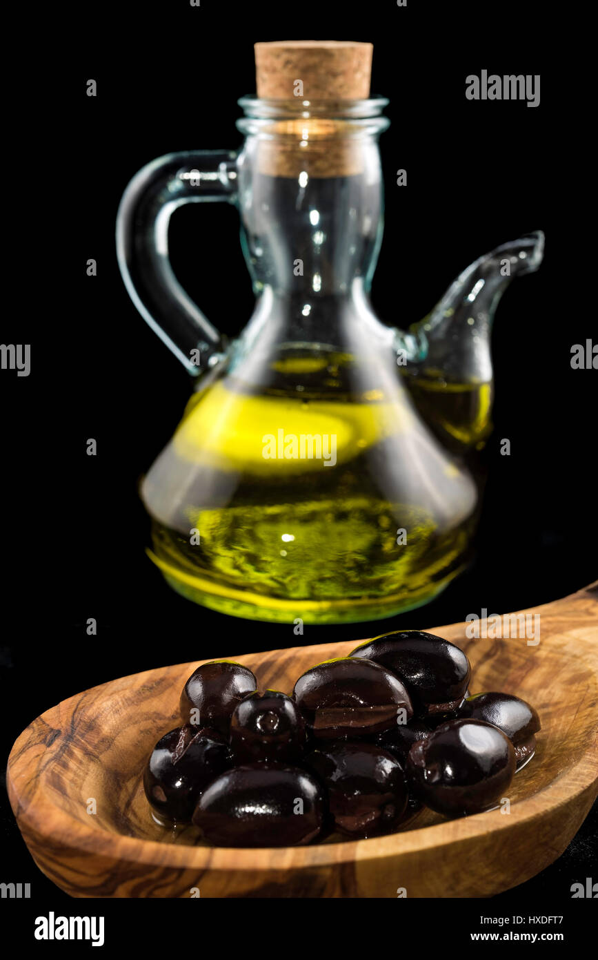 Black olives in wooden spoon and bottle of virgin olive oil on black ...