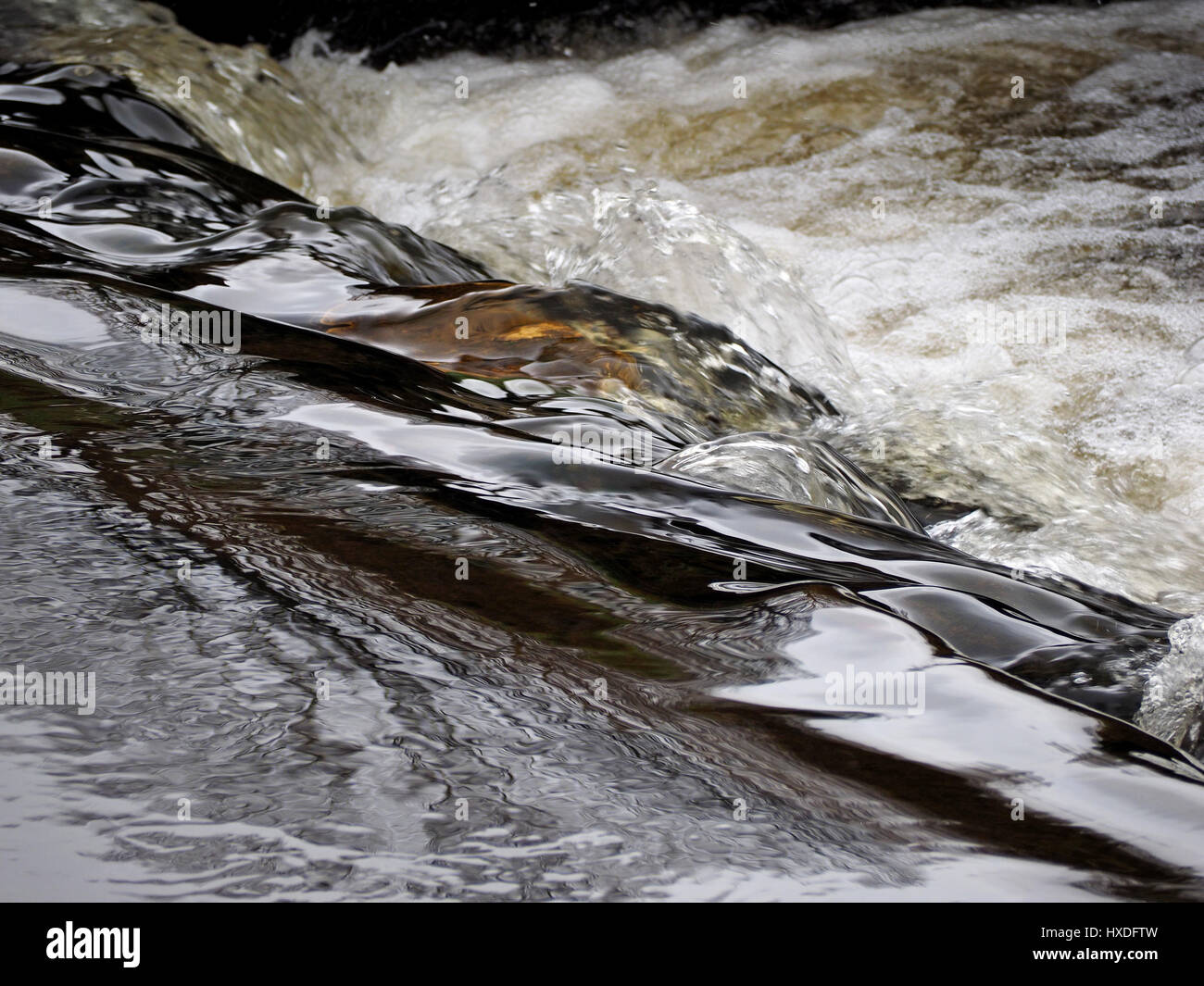 flowing water frozen in time at a waterfall giving contrast between smooth dark metallic liquid before it crashes into a foaming cascade of bubbles Stock Photo