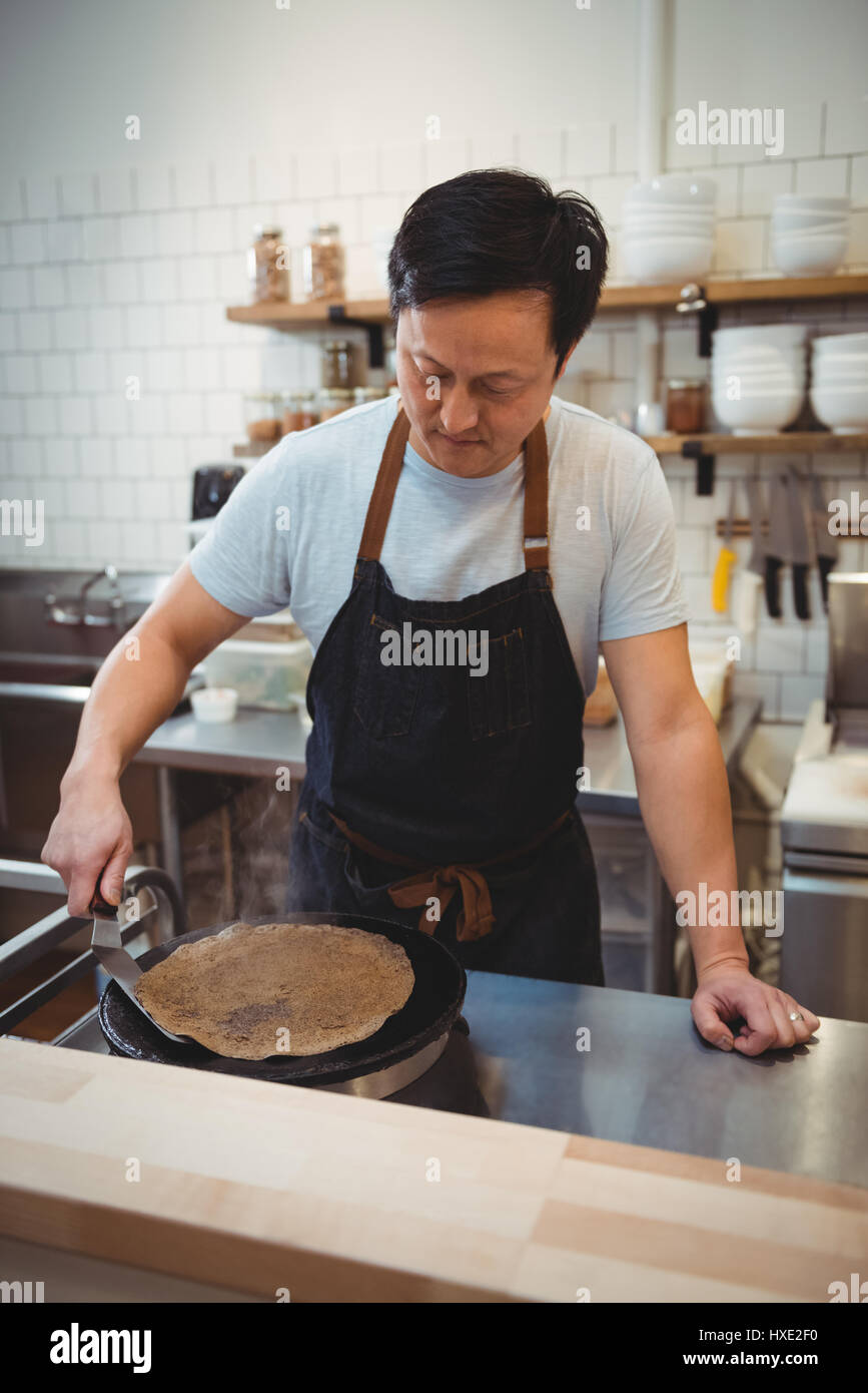 Male chef making pancake on frying pan in professional kitchen Stock