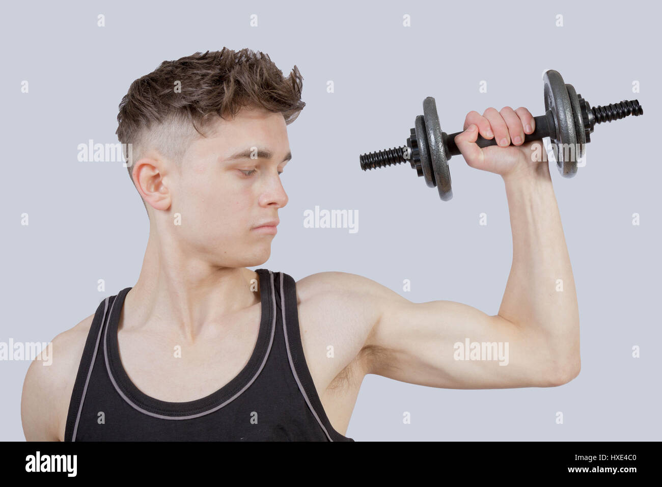 Strong teenage boy exercising by lifting weights Stock Photo