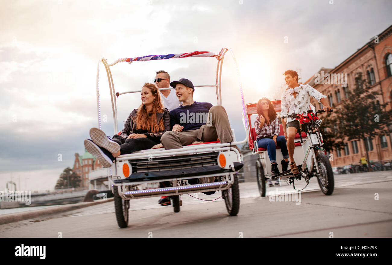 Group of young people enjoying tricycle ride in the city. Smiling friends sitting on tricycles on road. Stock Photo