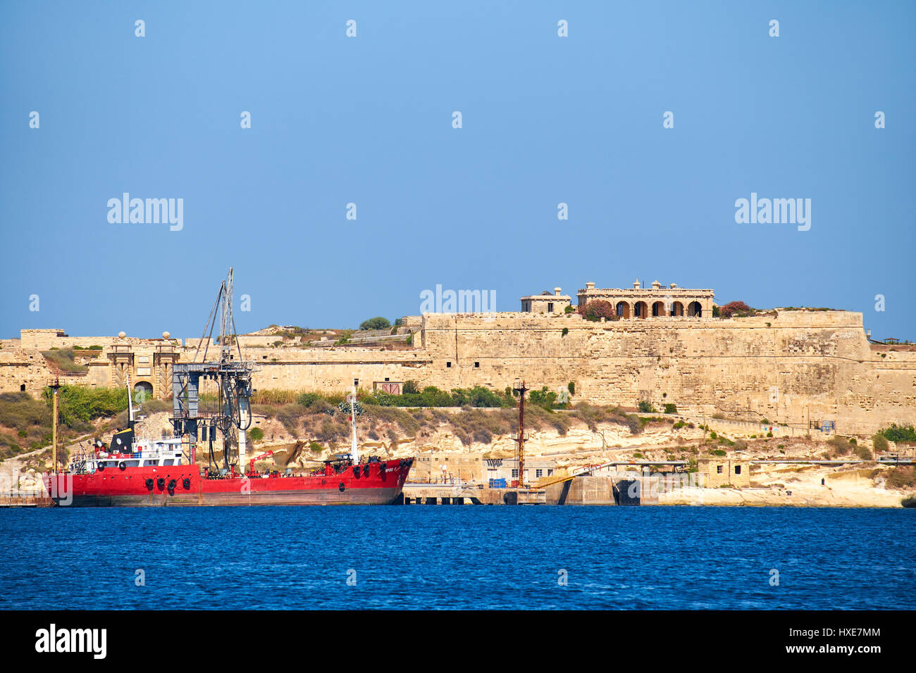 Kalkara, MALTA - JULY 24, 2015:  The cargo ship moored in the harbor of  Rinella Bay near the Fort Ricasoli, Kalkara, Malta Stock Photo